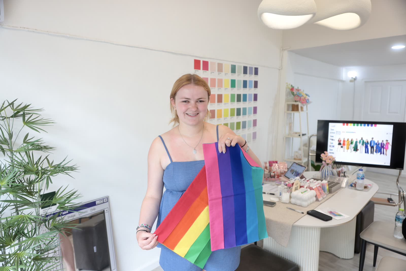Client holding her rainbow color drape fan next to the studio's Pantone wall